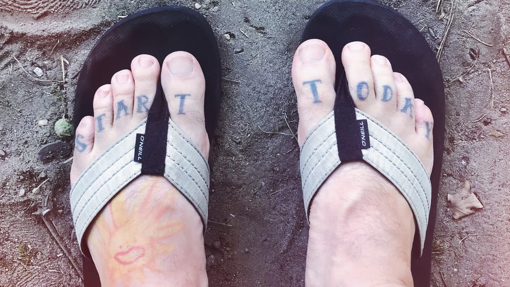 Füße in FlipFlops, auf den Zehen Tattoo "Start Today"