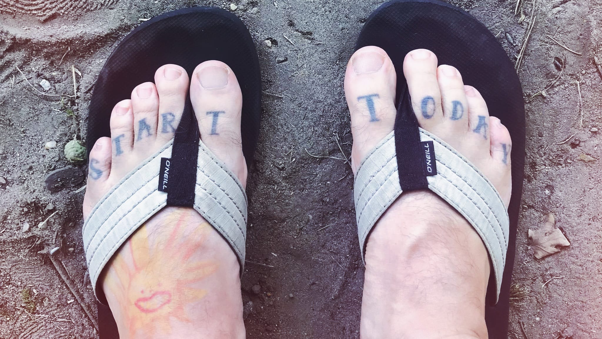 Füße in FlipFlops, auf den Zehen Tattoo "Start Today"